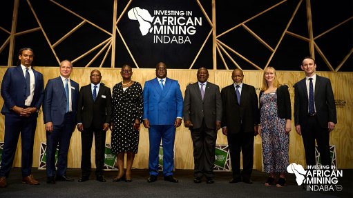 A group of men and ladies standing on a stage with the Investing in African Mining Indaba logo on a wall behind them at the indaba last year
