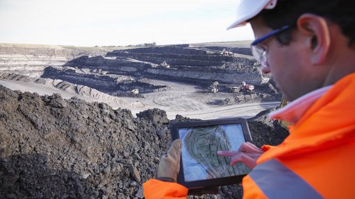 A man at an opencast mining operation wearing PPE working on geotechnical mapping on a tablet