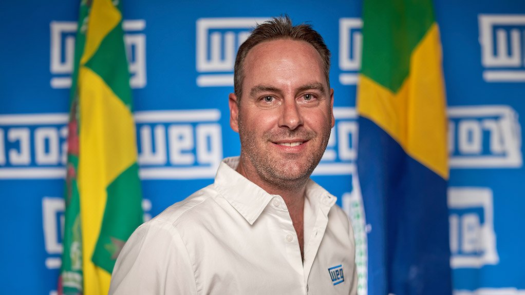 Man, white shirt, smiling in front of WEG logos