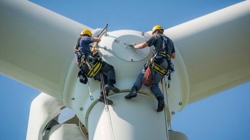 Two men wearing PPE and safety harnesses working on teh turbines of a wind turbine stack