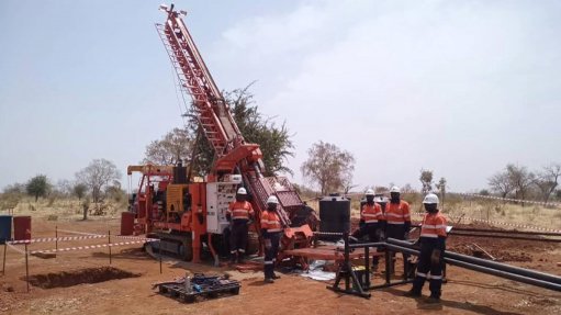 A core drill rig set in the Bakassi Zone 1 Drill area in Cameroon with five men in PPE around it