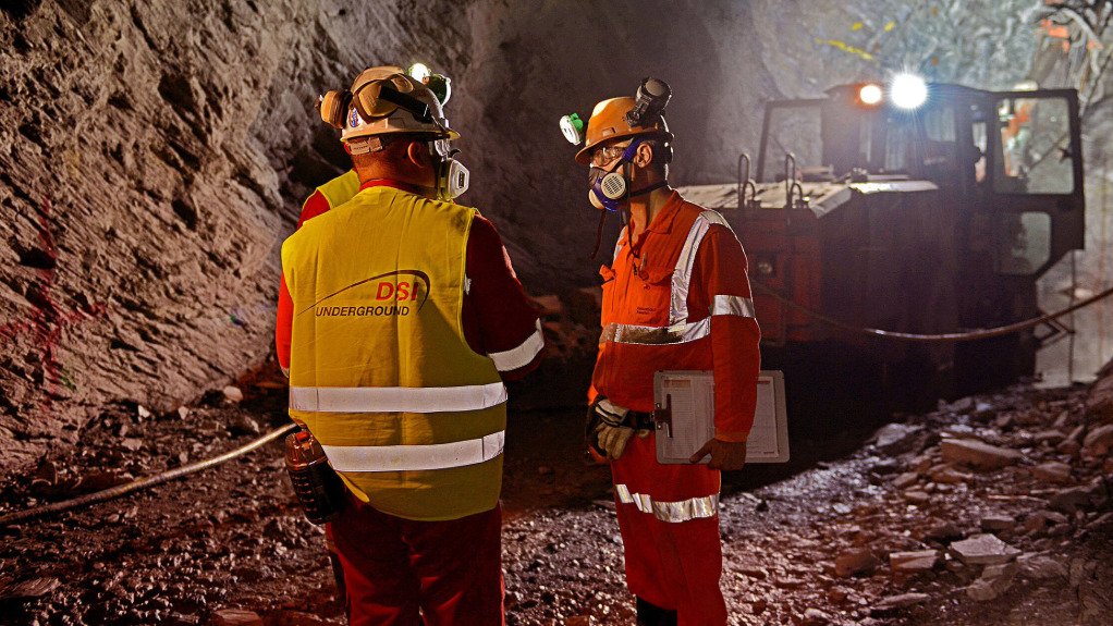 Three men in PPE in an underground tunnel discussing something in front of a borer