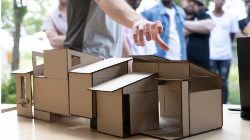 A cardboard cut out of the design of a modular building with a hand hovering over it