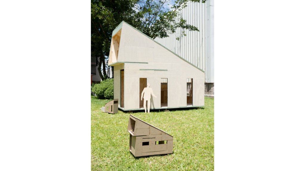 
A cardboard modular building on front of a constructed wood structure built to scale
