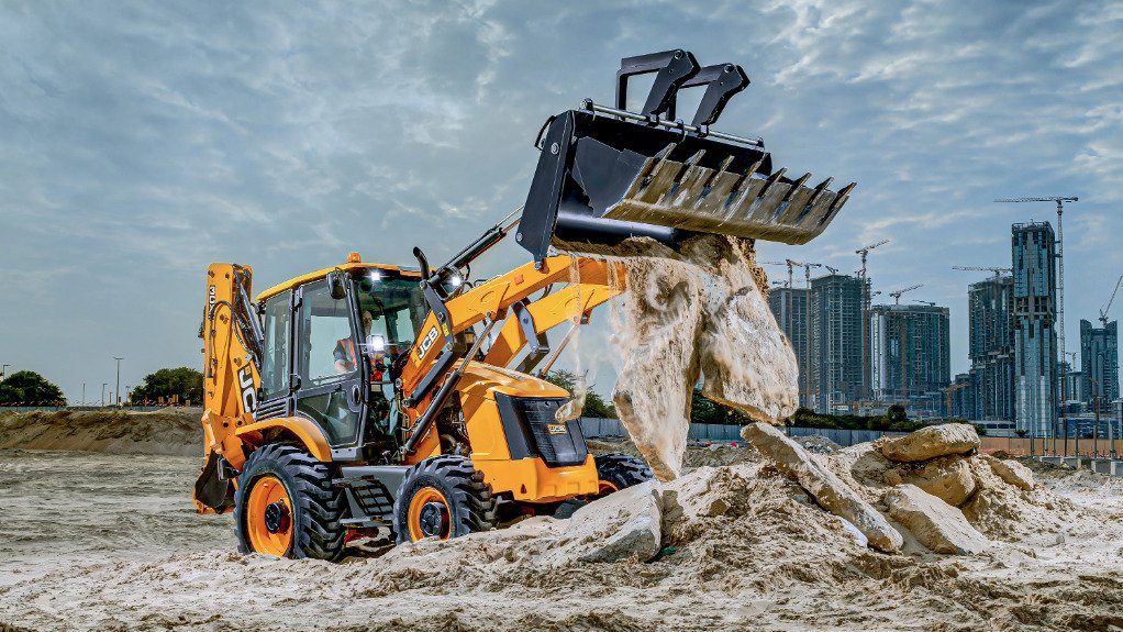 A  JCB 3CX backhoe loader on a construction site pouring sand from its bucket