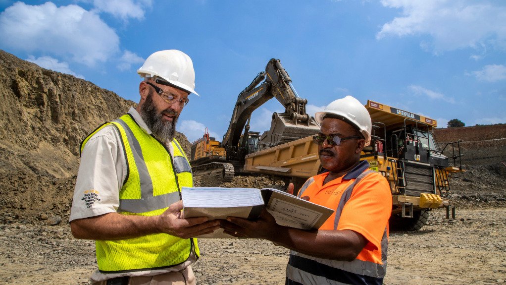 Two men in PPE stood looking at a contract in front of yellow machinery