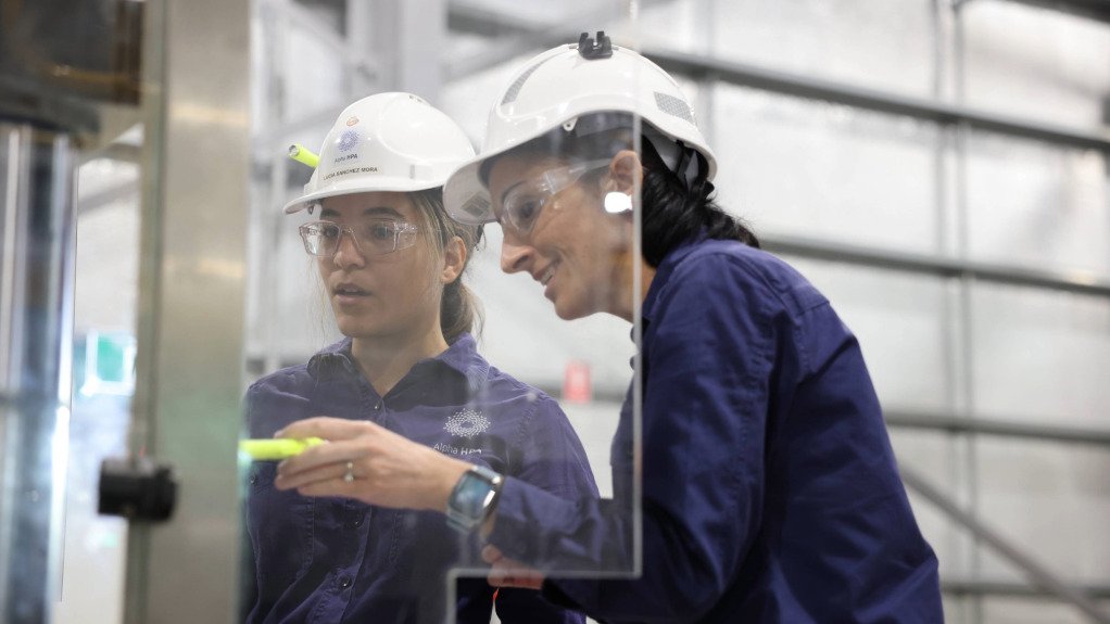 Two women in PPE and blue overalls working on a processing machine