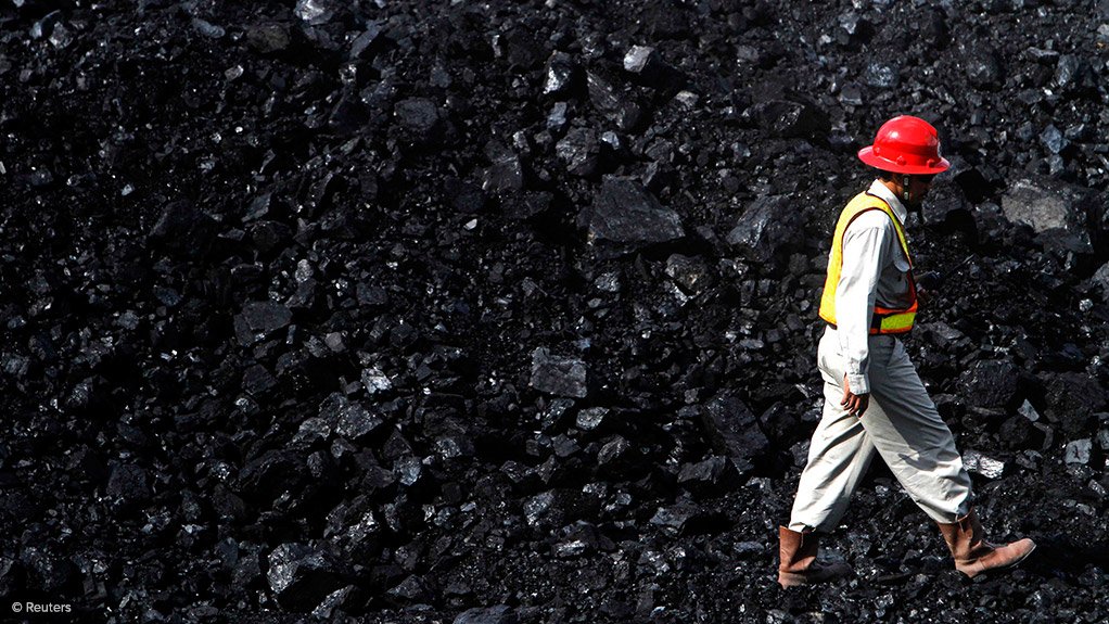 worker in PPE walking along coal stoockpile