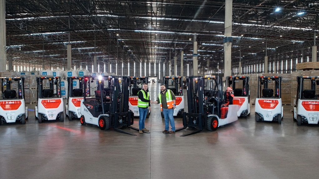 Two gents shaking hands in front of a fleet of Bobcat lithium-ion (Li-ion) forklifts