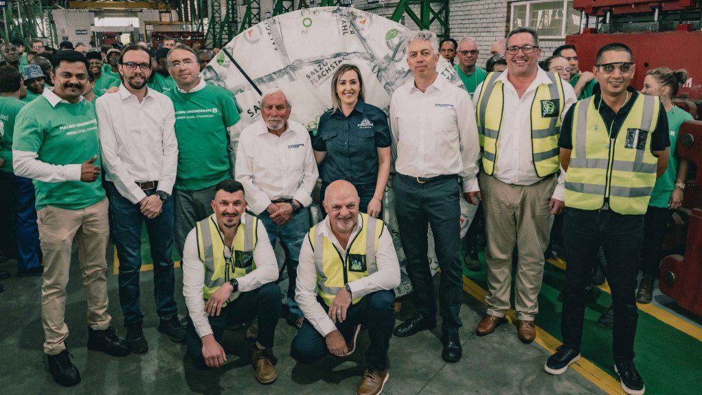 Malben Engineering founder Amerigo Smargiasso (centre) in front of green steel coil, alongside (left to right standing) Jithin Kottikal, Giuliano Smargiasso, Luca Smargiasso, of Malben, with Lee-Ann Geyser, of Allied Steelrode, Marco Smargiasso and Werner Kapp, also of Malben, and Naacam CEO Renai Moothilal, with Shane Barnard of United Steel and Marius Schafer of Malben kneeling.