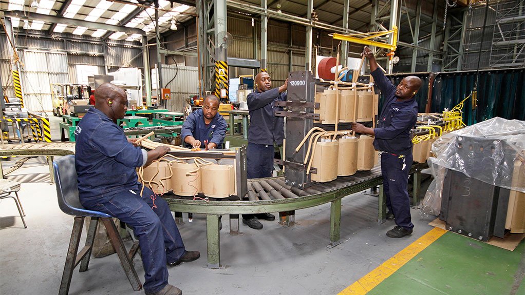 Distribution Transformers wiremen and tankers assembling components of NECRT auxiliaries in the division’s Knights factory. From left, Mbuso Sikhakhane connects delta on 22 kV auxiliary, Given Nedzamba mounts a copper link on a U-frame top for each core of the 22 KV auxiliary, Mothapisa Seetsi fastens a 33 kV auxiliary on its NEC U-frame and Ben Nalana connects NEC main leads with the 33 kV auxiliary