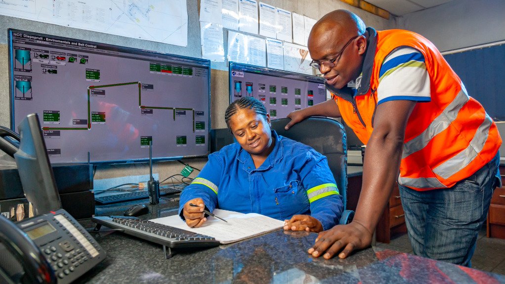 A woman sat at a desk with a man stood next to her explaining some finer details on shaft sinking