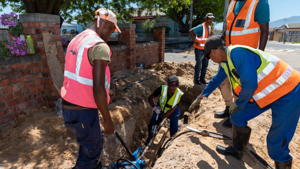 Three men wearing PPE working on the sntallation of a pipe in the ground in Cape Town