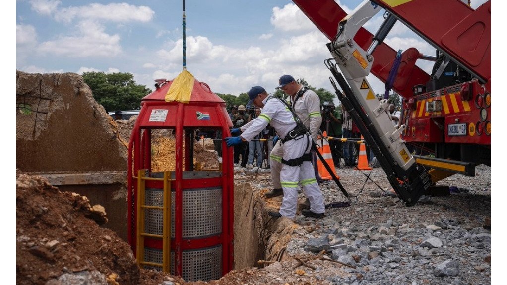 A large cage attached to a mobile rescue winder being manned by two men wearing PPE at the Buffelsfontein mine during a huge rescue operation.