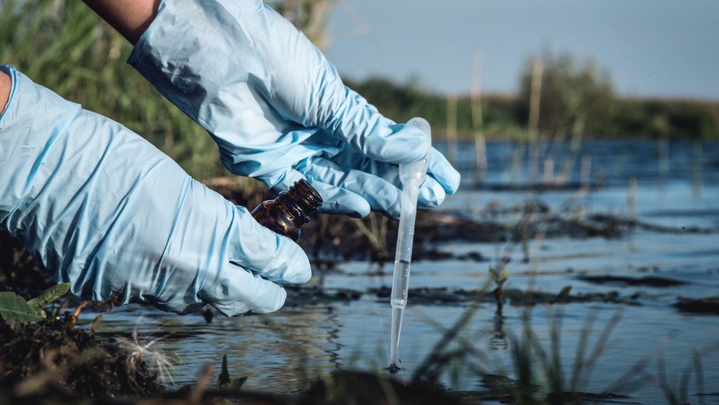 Image of scientist extracting water sample from polluted pond