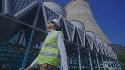 A man wearing PPE walking on front of Cooling towers looking up to the sky