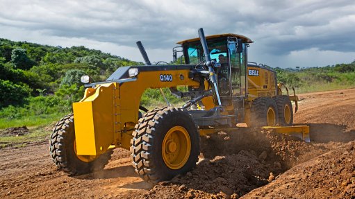 A large yellow grader made by Bell Equipment in the bush grading a road