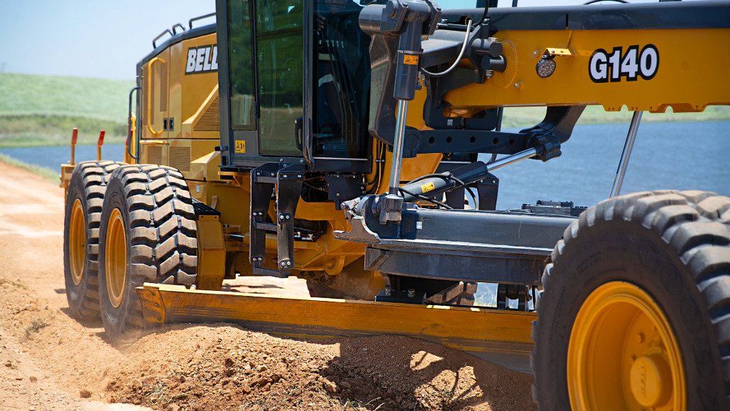 A yellow bell grader at work near a dam