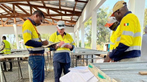 Four men in visi vests stood looking at samples under a tarp structure in the Bush 