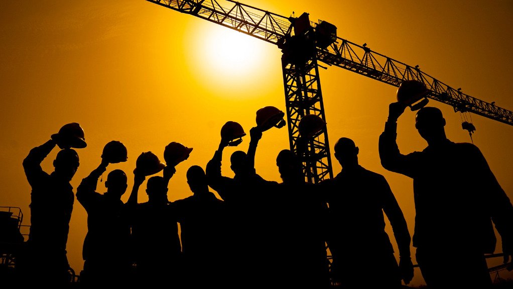miners raising their helmets against sunset and crane