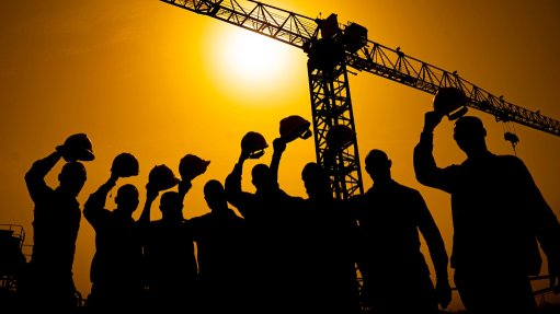 miners raising their helmets against sunset and crane