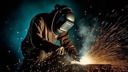 A welder in PPE welding a metal plate with pretty sparks flying everywhere