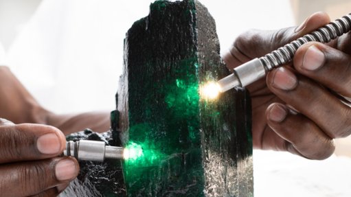 a large emerald being inspected by someone with two high powered torches projecting int the gemstone