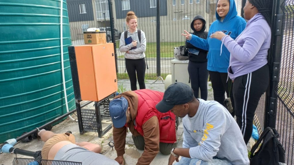 A grou of student stood at a borehole well with a JoJo tank and pumping system