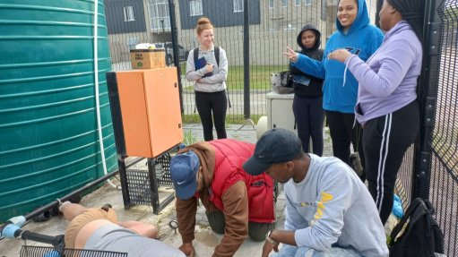A grou of student stood at a borehole well with a JoJo tank and pumping system