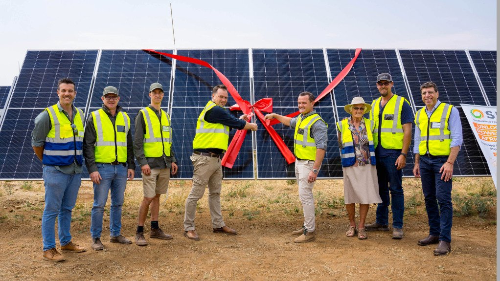 A group of people stood in front of a large solar panel cutting a large red ribbon to commemorate the commissioning of a solar plant.