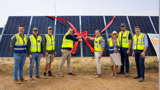 A group of people stood in front of a large solar panel cutting a large red ribbon to commemorate the commissioning of a solar plant.