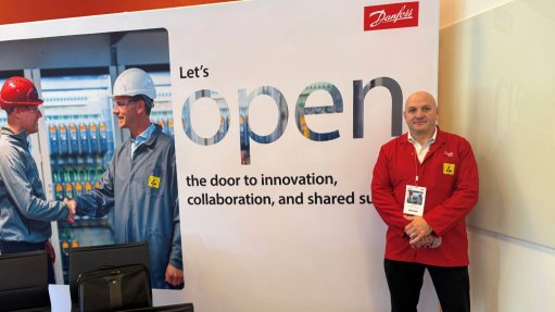 A man standing next to a poster where two men are shaking hands with the Danfoss logo on it