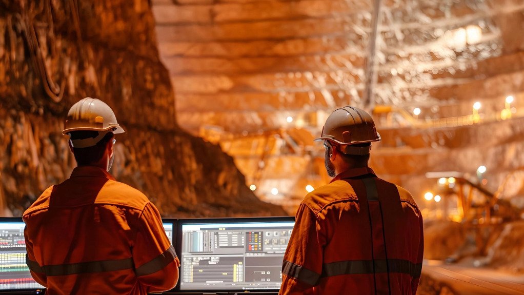 Two men in an underground mine wearing PPE and in front of screens