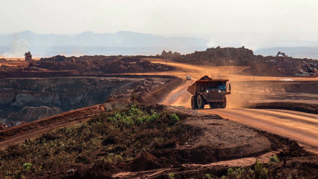 A large mining vehicle kicking up brown dust on a brownfield mining operation