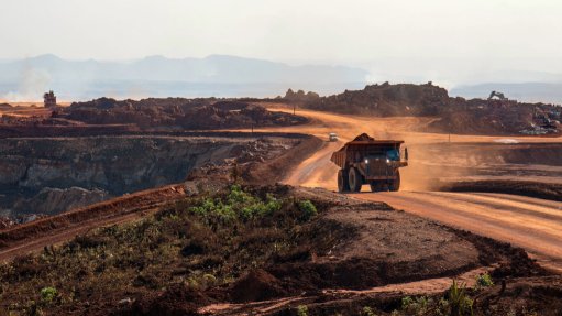 A large mining vehicle kicking up brown dust on a brownfield mining operation