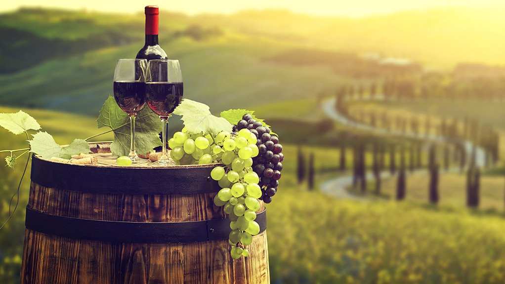A bottle of wine, glasses and grapes on a barrel at a winery