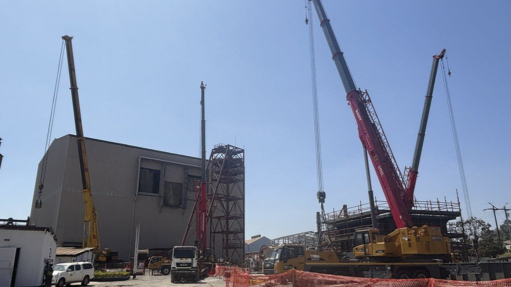 With the new winder house visible in the background, four mobile cranes lift steel sections for the pre-assembly of the headgear