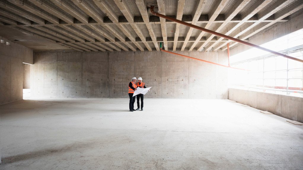 The above image depicts two project managers looking at blueprints for a building