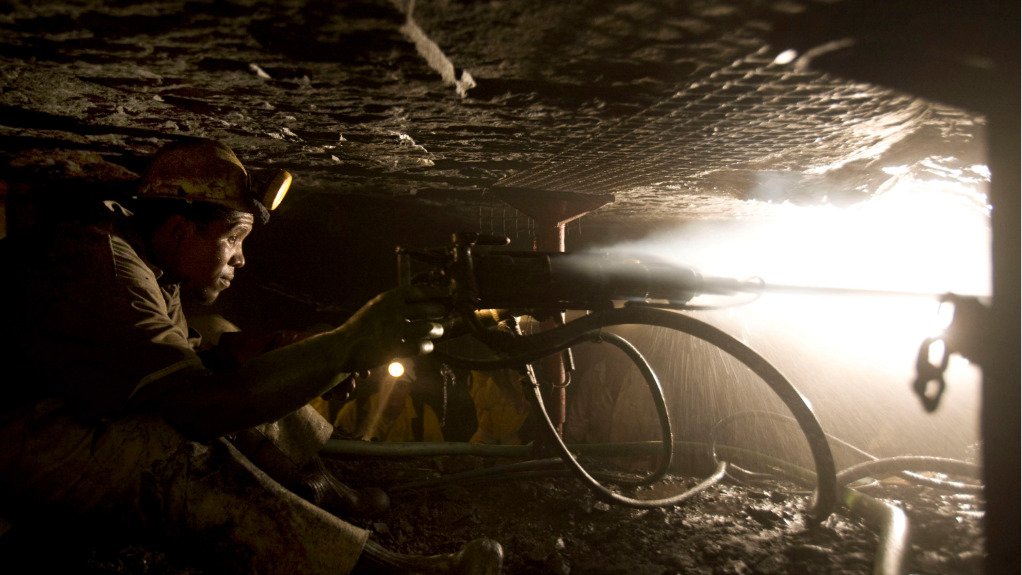 A man underground wearing hard hat and light operating a hand drill