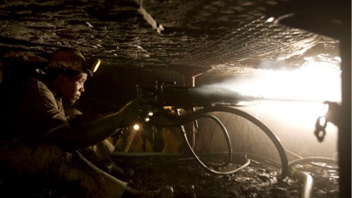 A man underground wearing hard hat and light operating a hand drill